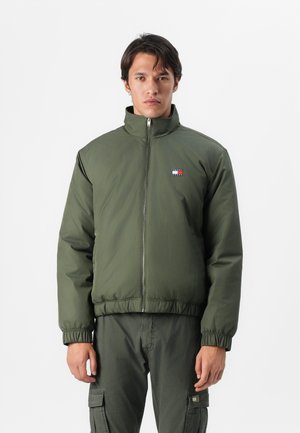 Olive green zip-up jacket with high collar, elasticized cuffs, and hem. Features a logo patch in red, white, and blue on the chest.