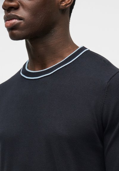 Pull bleu foncé avec un col rond bordé d'un liseré bleu clair. Le tissu semble lisse et ajusté, mettant en valeur la texture.