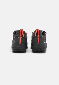 Sorte trail sko med røde accenter, med en åndbar mesh-overdel, en robust gummisål og et greb-forbedrende dækmønster.