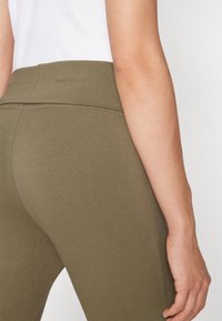 Maslinaste tajice od mekog, rastezljivog materijala s glatkom teksturom i širokim pojasom koji sadrži suptilni logotip.