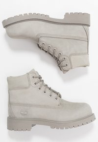 Stivali alla caviglia in suede grigio con punta arrotondata, sei asole e suola spessa scanalata. Il design include dettagli cuciti e un logo.