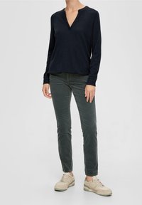 Marinblå långärmad skjorta med V-hals, ihopparad med mörkgröna slim-fit byxor och krämfärgade sneakers med gröna accenter.