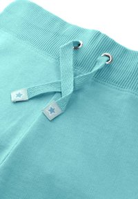 Turkusowe spodnie dresowe z żebrowanym paskiem w talii, z metalowymi oczkami w kolorze srebrnym i sznurkiem z akcentem gwiazdek. Miękka faktura tkaniny, swobodny design.