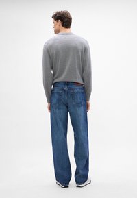 Maglietta grigia a maniche lunghe abbinata a jeans in denim blu dal taglio morbido. I jeans presentano tasche posteriori e un'etichetta in pelle sulla vita.