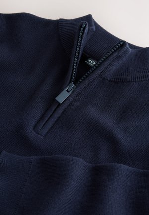 Marineblauer Pullover aus Strickstoff mit Viertel-Reißverschluss vorne, geripptem Kragen und dezent strukturierter Oberfläche. Der Reißverschlussanhänger ist matt schwarz.