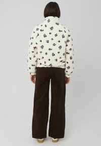 Veste en polaire blanche avec un motif floral violet et marron, col haut et taille élastique, associée à un pantalon en velours côtelé marron.