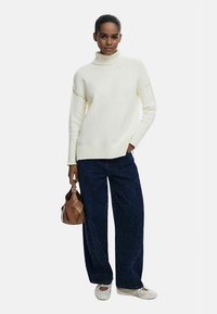 Kremfarvet rullekravetrøje med ribkant ved ærmerne, kombineret med mørkeblå viddebukser med diskrete glimmerdetaljer. Brun håndtaske med vævet design.