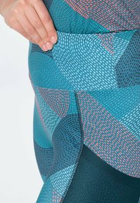 Sportieve leggings met een geometrisch patroon in turquoise, koraal en marineblauw. Het materiaal heeft een zachte textuur met contrasterende secties en stiksels.