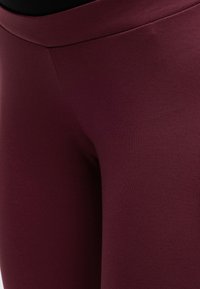 Gros plan sur un legging extensible bordeaux montrant un tissu lisse et des détails de couture autour de la taille et de la partie supérieure de la cuisse.
