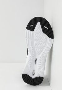 Semelle de sneaker noir et blanc en caoutchouc texturé, avec un design hybride, un motif en losange et un détail de logo près du talon.