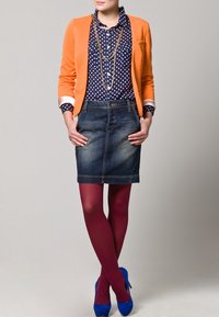 Blazer naranja sobre una camisa de lunares azul marino, combinado con una falda de mezclilla, medias granate y tacones altos azules. Un collar dorado añade detalle.
