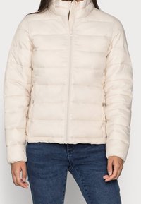 Světlá béžová péřová bunda s vysokým límcem, horizontálním prošíváním, zipovým uzávěrem a bočními kapsami. Měkká textura, vhodná pro chladnější počasí.