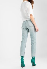 Jean taille haute bleu clair à coupe droite, avec un ourlet brut. Associé à des bottines vertes à bout pointu.