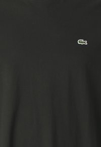 Černé bavlněné tričko s malým vyšívaným zeleno-bílým logem na hrudi. Krátké rukávy a kulatý výstřih. Měkká textura.