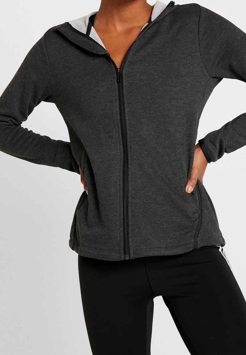 Sweat à capuche gris à fermeture éclair avec une doublure intérieure contrastante blanche. Il présente des manches longues, des poches latérales et une coupe ajustée, fabriqué dans un matériau doux.