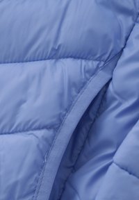 Intérieur d'une veste en nylon légère de couleur bleu clair, présentant un motif matelassé, une texture lisse et une bordure en tissu contrastant le long du bord.