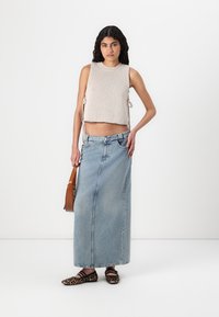 Débardeur tricoté beige clair avec des liens sur les côtés, associé à une longue jupe en denim bleue et des ballerines noires à imprimé léopard. Sac à dos marron.