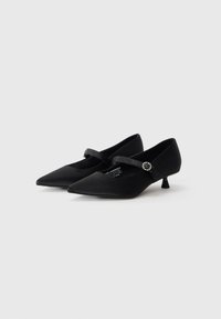 Zapatos negros de punta con acabado satinado, que presentan un delgado tacón de gatito y una tira decorativa con una hebilla redonda de plata.