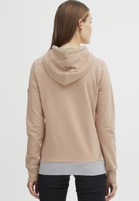 Light pink hooded sweatshirt with a gray hem, soft texture, long sleeves, and logo detail on the back. Simple, modern design.
