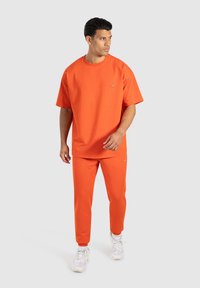 Orange bomullströja och matchande sweatpants. T-shirten har rund hals och korta ärmar; sweatpants har resår i midjan.
