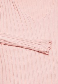 Lichtroze geribde trui met een V-hals ontwerp, met lange mouwen en textiele stof. De mouw loopt langs de zijkant van de trui.