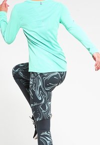 En tætsiddende, langærmet mintgrøn træningstop parret med sorte leggings med et virvlende marmor mønster i lyseblå accenter.