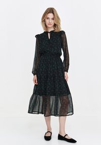 Black floral midi dress with ruffled neckline, long sheer sleeves, gathered waist, and tiered skirt with a semi-transparent overlay.