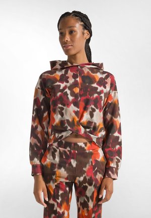 Hooded sweatshirt with an abstract pattern in brown, orange, and cream. Features a knotted front and paired with matching pants.