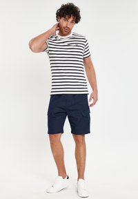 Stribet sort og hvid t-shirt med rund hals, parret med marineblå cargo shorts med sidelommer og hvide sneakers.