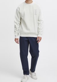 Jasnoszary sweatshirt z okrągłym dekoltem i subtelnym napisem po lewej stronie. Połączony z granatowymi spodniami i białymi trampkami. Gładka tekstura.