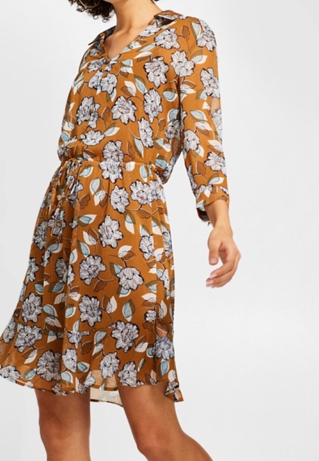 Femme portant une robe marron à fleurs blanches et bleues, manches trois-quarts et taille cintrée avec un cordon.