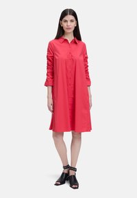 Robe chemise rouge à boutons, avec col, manches longues et ourlet évasé. Portez avec des chaussures ouvertes noires à bout découvert avec des brides de cheville.
