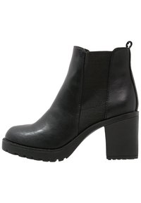 Botte de cheville en cuir noir avec un talon bloc épais, des panneaux latéraux élastiques et une surface texturée. Elle dispose d'un passant à l'arrière.