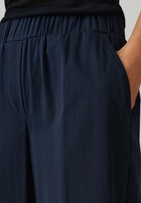 Navyblauwe, lichte broek met een gladde textuur, een elastische tailleband en zijzakken, getoond van de taille tot halverwege de bovenbenen.