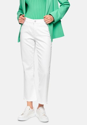 White cropped jeans with frayed hem, paired with a green ribbed top and a green blazer. Features white sneakers with gold accents.