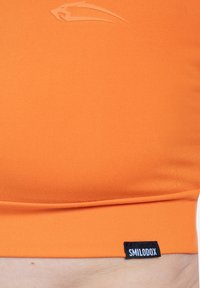 Oranje tanktop van een glad, rekbaar materiaal. Voorzien van een subtiel merklogo en een zwart label aan de zoom. Eenvoudig design, nauwsluitende pasvorm.