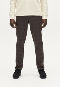 Pantaloni a quadri marroni realizzati in tessuto testurizzato, abbinati a una camicia a maniche lunghe crema e scarpe nere, visti dalla vita in giù.