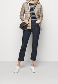 Beige puffig jacka, marinblå och vitrandig topp, mörka jeans i kort modell, vita sneakers och en liten svart axelremsväska med gulddetaljer.