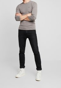 Graues Langarmshirt mit Rundhalsausschnitt, kombiniert mit schwarzen Jeans und weißen High-Top-Sneakern. Einfaches, schmal geschnittenes Design mit sichtbaren Nähten.