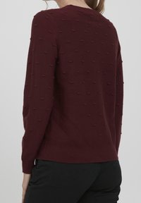 Burgunder farbener Pullover mit strukturierten Knopfdetails, Rundhalsausschnitt und langen Ärmeln. Strickstoff und gerippter Saum sowie Bündchen. Minimalistisches Design.