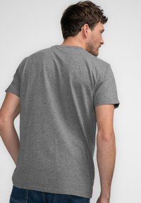 Camiseta gris de manga corta con cuello redondo y corte estándar, hecha de una tela suave y texturizada. El diseño presenta una espalda limpia y simple.