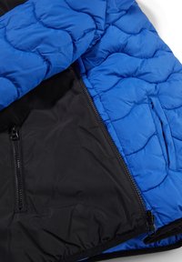 Blåt quiltet jakkeinteriør med sort foer, der har en lynlås lomme og synligt syningsmønster. Glat tekstur, holdbart materiale.