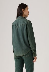 Groen denim shirt met lange mouwen, een spitse kraag en contrasterende stiksels. Heeft een yoke-ontwerp op de achterkant en knoopmanchetten.