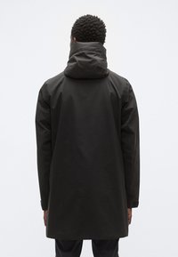 Μακρύ, μαύρο αδιάβροχο με ψηλό γιακά και κουκούλα. Λείο, αδιάβροχο υλικό. Διαθέτει μακριά μανίκια με ρυθμιζόμενες μανσέτες.