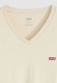 Beige V-nyakú pamut póló. Az alsó bal oldalon egy kis piros Levi's logó embléma található. Puha tapintású, klasszikus fazonú.