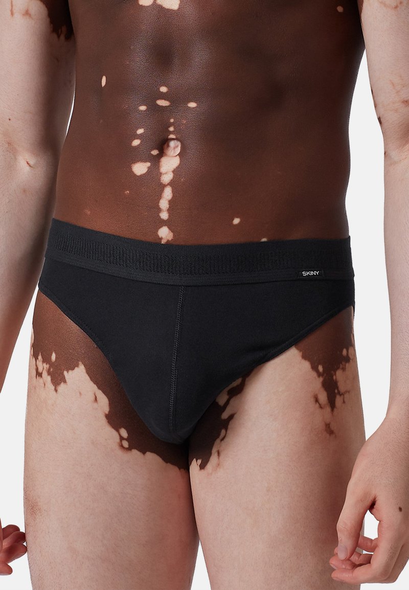 Slip in cotone nero con un'ampia fascia elastica in vita, caratterizzati da una superficie liscia e dettagli di cucitura minimali sui lati.