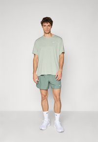 T-shirt de sport vert clair et shorts assortis, tous deux en matière douce, avec un logo Nike blanc sur la poitrine et sur les shorts. Baskets blanches.
