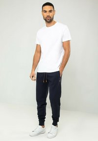 Weißes Rundhals-T-Shirt kombiniert mit marineblauen Sweatpants, die eine orangefarbene Kordel und seitliche Taschen haben, ergänzt durch weiße Sneakers.