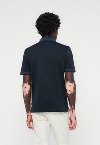 Polo de marinha com um acabamento texturizado. Apresenta um colarinho em contraste e detalhes nas mangas. Corte clássico com fendas laterais na bainha.