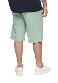 Shorts vert clair en coton, à coupe droite, tombant juste au-dessus du genou, associés à des baskets blanches.